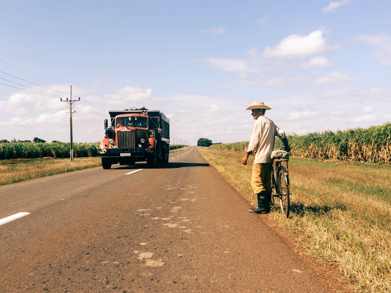 Services A rural scene with a farmer beside his bicycle and an oncoming vintage truck on an open road.