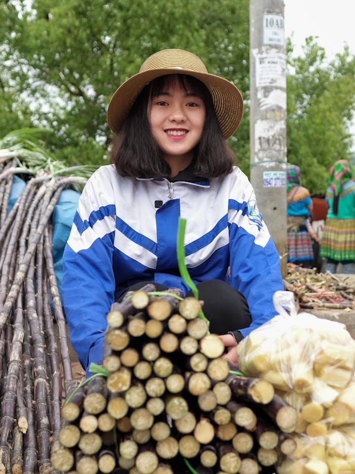 About Portrait of a smiling woman at a Vietnamese market with sugarcane and produce.